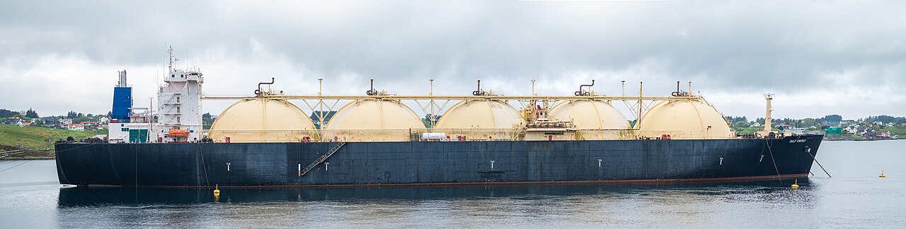 An LNG tanker at anchor in a Norwegian strait, its spherical-looking tanks and blue hull visible against the coast.