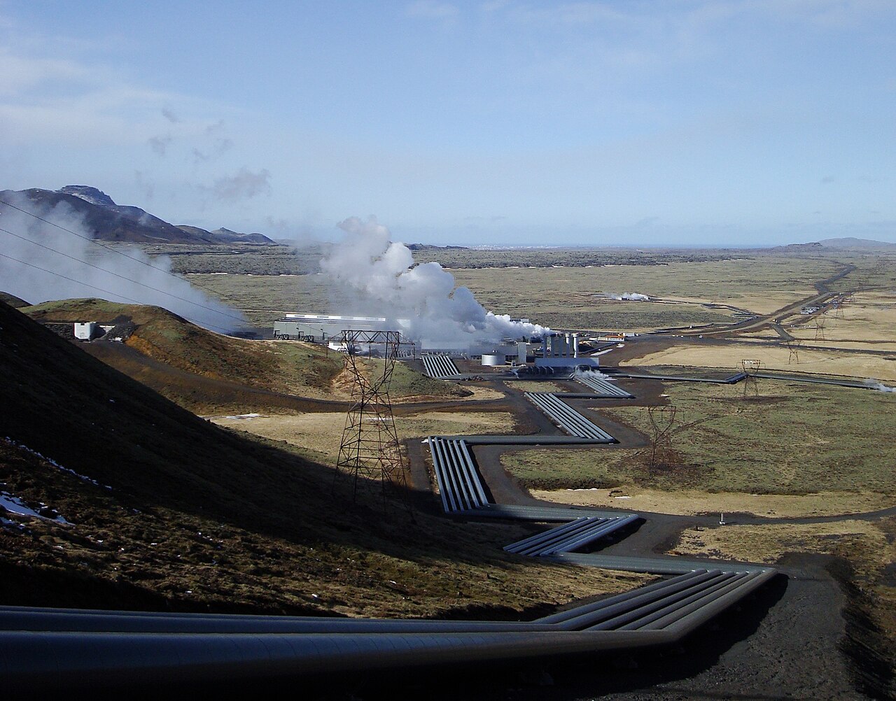 Hellisheiði geothermal power station in Iceland, buildings and steam on a mossy plain.