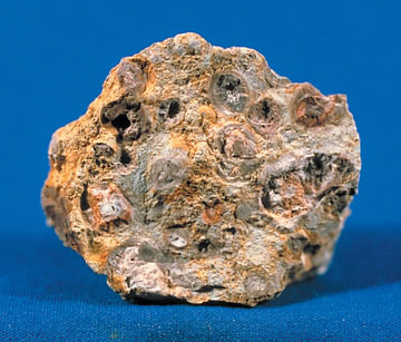 A specimen of bauxite, a porous tan rock, on a blue cloth.